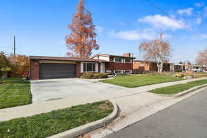 Split level home featuring concrete driveway, brick siding, a garage, a chimney, and a front yard