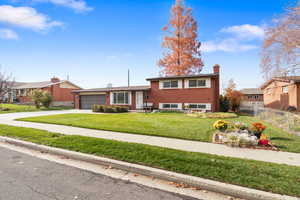 View of front of property featuring a chimney, brick siding, concrete driveway, and a garage