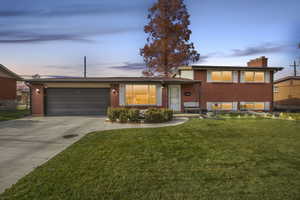 Tri-level home featuring brick siding, a yard, driveway, and a chimney