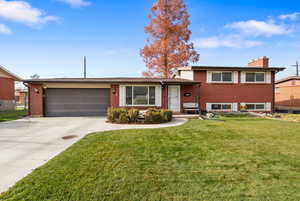 Split level home featuring brick siding, a chimney, driveway, and a front lawn
