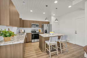 Kitchen featuring light stone counters, brown cabinetry, a center island, stainless steel appliances, and decorative backsplash