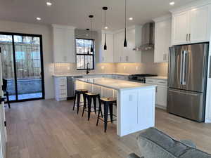 Kitchen featuring appliances with stainless steel finishes, light wood-type flooring, wall chimney range hood, a breakfast bar, and recessed lighting