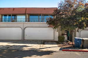 View of front facade with concrete driveway, a tile roof, stucco siding, and a balcony