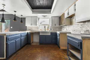 Kitchen featuring a tray ceiling, blue cabinets, decorative backsplash, concrete floors, and wooden ceiling