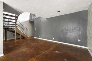 Unfurnished living room with concrete floors, stairs, and a textured ceiling