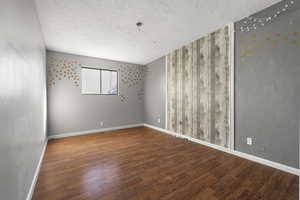 Spare room featuring a textured ceiling, wood finished floors, and a textured wall