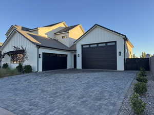 Modern inspired farmhouse with board and batten siding, an attached garage, decorative driveway, and brick siding