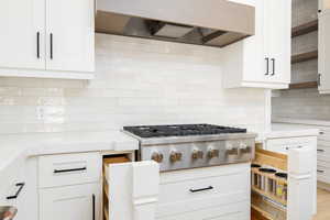 Kitchen with exhaust hood, white cabinets, light stone counters, and stainless steel gas stovetop