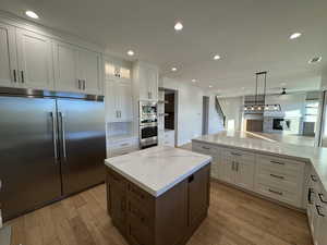 Kitchen with white cabinetry, a fireplace, built in appliances, a kitchen island, and recessed lighting