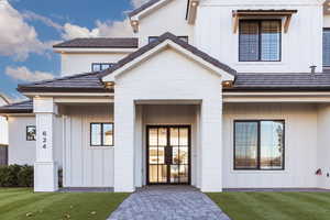 View of exterior entry with board and batten siding, a lawn, brick siding, and a porch