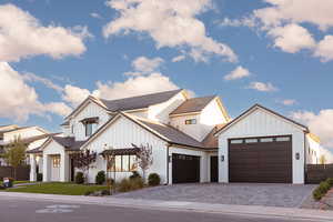 Modern inspired farmhouse with board and batten siding, decorative driveway, an attached garage, and brick siding