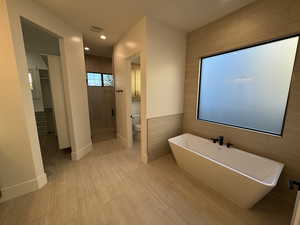 Full bathroom with a stall shower, a soaking tub, a walk in closet, recessed lighting, and tile walls