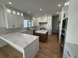 Kitchen with white cabinetry, light wood finished floors, glass insert cabinets, light stone countertops, and stainless steel appliances