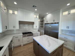 Kitchen featuring glass insert cabinets, a kitchen island, stainless steel appliances, white cabinets, and light stone counters