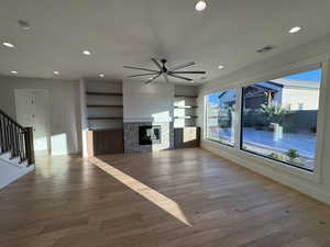 Unfurnished living room featuring built in features, a stone fireplace, light wood-style floors, recessed lighting, and stairs