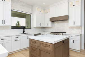 Kitchen featuring white cabinetry, light stone counters, glass insert cabinets, backsplash, and recessed lighting