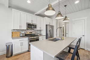 Kitchen featuring appliances with stainless steel finishes, white cabinetry, a breakfast bar, light wood finished floors, and recessed lighting