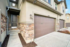 Doorway to property with stone siding, stucco siding, a garage, and concrete driveway