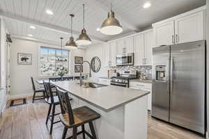 Kitchen with stainless steel appliances, white cabinets, a kitchen island with sink, a breakfast bar area, and decorative backsplash