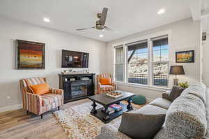 Living area featuring wood finished floors, a glass covered fireplace, a ceiling fan, and recessed lighting