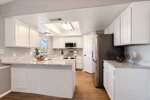 Kitchen featuring white cabinets, a peninsula, light stone counters, stainless steel appliances, and light wood finished floors