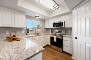 Kitchen featuring stainless steel appliances, light stone countertops, white cabinetry, and a tray ceiling