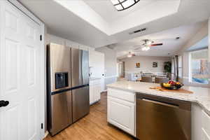 Kitchen featuring stainless steel appliances, light stone counters, white cabinetry, open floor plan, and lofted ceiling