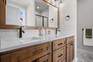 Bathroom with light marble finish flooring, double vanity, and a stall shower