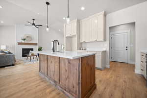 Kitchen with decorative light fixtures, a fireplace, a kitchen island with sink, vaulted ceiling, and open floor plan