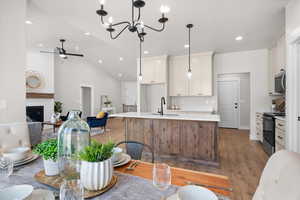 Kitchen featuring white cabinetry, range with electric stovetop, vaulted ceiling, light wood-style flooring, and a center island with sink