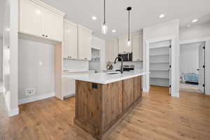 Kitchen with a center island with sink, hanging light fixtures, stainless steel appliances, light wood-style floors, and brown cabinets