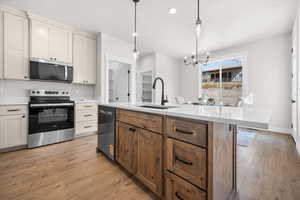 Kitchen featuring stainless steel appliances, a chandelier, hanging light fixtures, brown cabinets, and light wood-style floors