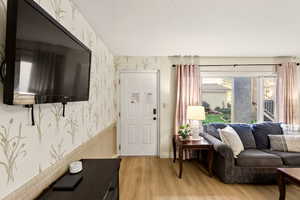 Living room with wallpapered walls, a wainscoted wall, light wood-style floors, and a textured ceiling