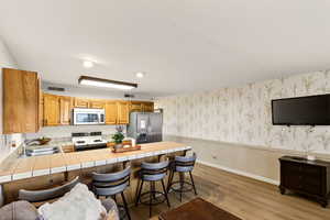 Kitchen with wallpapered walls, a wainscoted wall, a kitchen bar, a peninsula, and stainless steel appliances