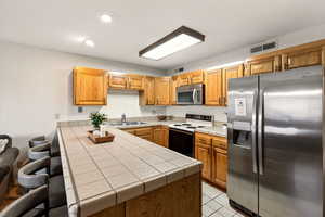 Kitchen featuring wallpapered walls, appliances with stainless steel finishes, a kitchen breakfast bar, tile countertops, and a peninsula