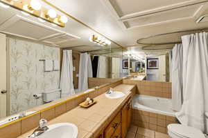 Bathroom featuring tiled tub, double vanity, curtained shower, and light tile patterned floors