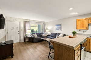 Kitchen with wallpapered walls, tile counters, open floor plan, a kitchen breakfast bar, and brown cabinets