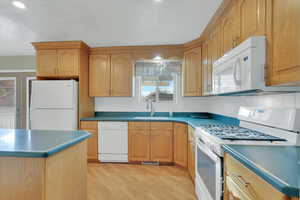 Kitchen featuring white appliances, tasteful backsplash, light wood-type flooring, and dark countertops