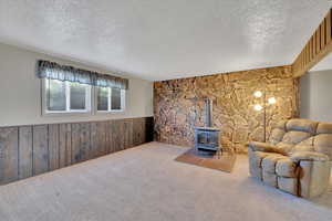 Living area featuring a wood stove, wood walls, a textured ceiling, a wainscoted wall, and carpet floors