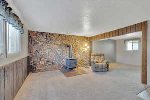 Sitting room with a wood stove, a textured ceiling, wood walls, and carpet flooring