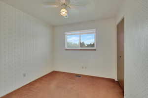 Empty room featuring wallpapered walls, carpet, and a ceiling fan