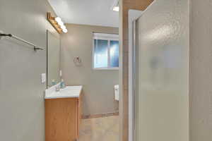 Full bath with vanity, a stall shower, light tile patterned floors, and a textured wall