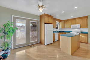 Kitchen featuring white appliances, a kitchen island, light wood finished floors, decorative backsplash, and recessed lighting
