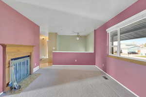Unfurnished living room with carpet flooring, ceiling fan, and a fireplace with flush hearth