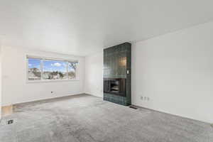 Unfurnished living room with a tiled fireplace and carpet floors