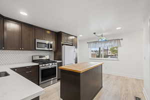 Kitchen with dark brown cabinetry, appliances with stainless steel finishes, backsplash, a center island, and butcher block counters