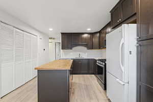 Kitchen with wood counters, freestanding refrigerator, dark brown cabinets, stainless steel range with gas stovetop, and light wood-style flooring