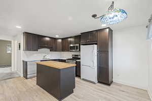 Kitchen featuring dark brown cabinetry, wooden counters, stainless steel appliances, a center island, and light wood-style flooring