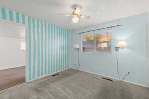 Carpeted spare room featuring a ceiling fan, a textured ceiling, and wallpapered walls