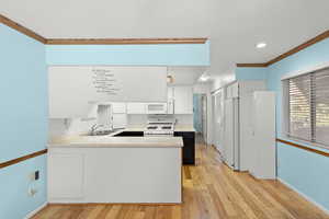 Kitchen with white cabinets, light countertops, crown molding, a peninsula, and white appliances